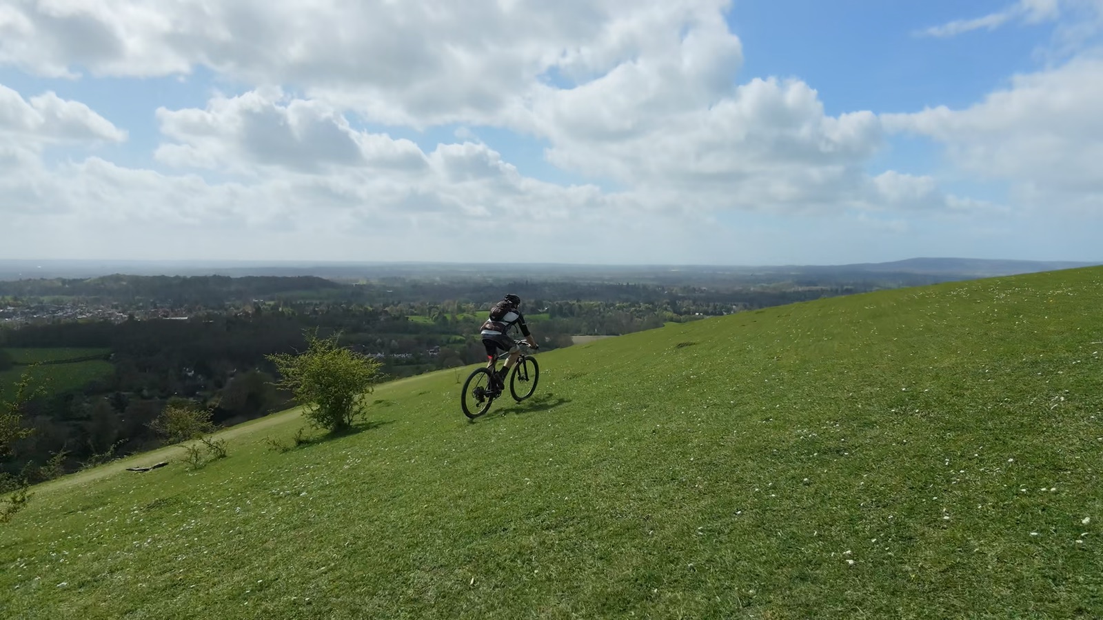 Drone view of a mountain biker crossing an open green hillside at Mogador